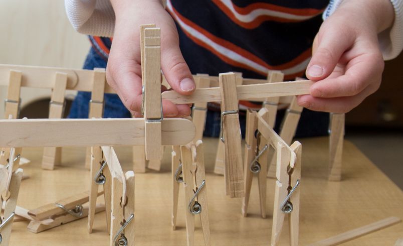 Kinderhände, die etwas aus Wäscheklammern und Eisstielen bauen